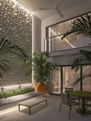 A modern interior with a high ceiling, a ceiling fan, a large window with a view, a green sofa, a dining table with chairs, and a large potted plant. - Alma Suites Heraklion (Iraklio)
