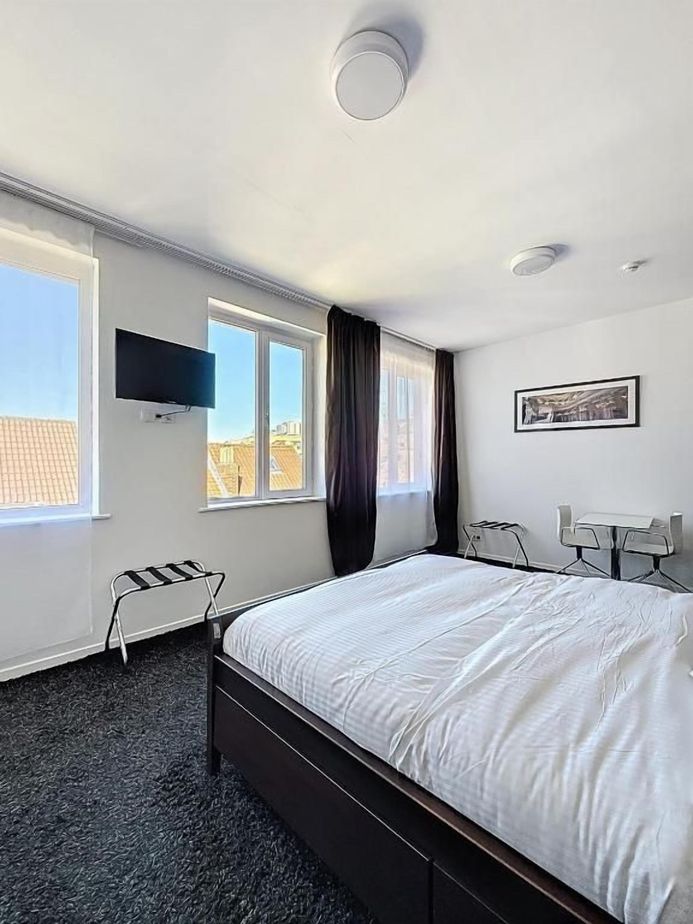 Une chambre d’hôtel comprenant un lit, un téléviseur à écran plat, un bureau avec une chaise et une fenêtre avec des rideaux.