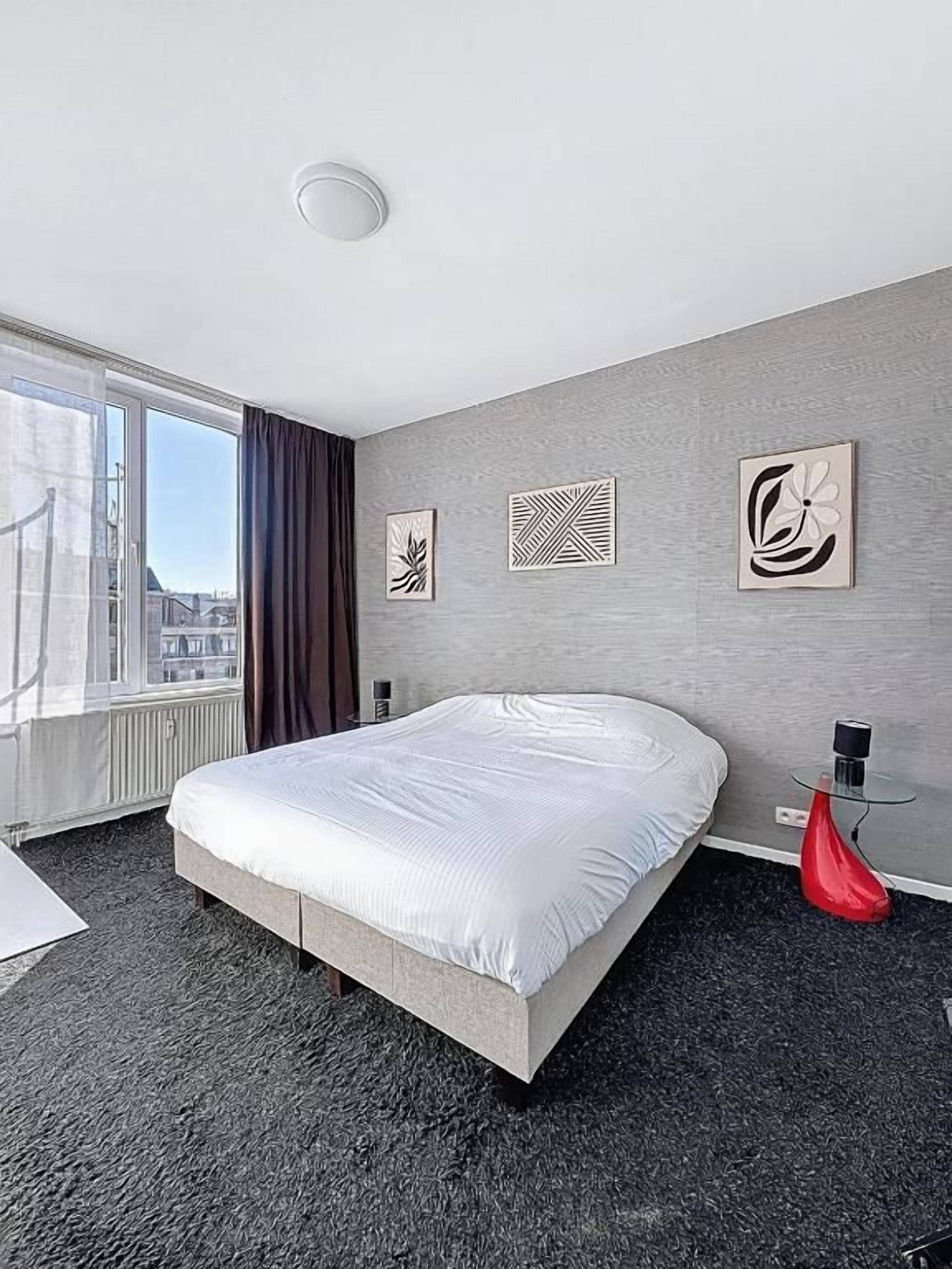 Une chambre d’hôtel avec un grand lit, une fenêtre avec des rideaux et des œuvres d’art accrochées au mur.