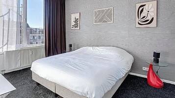 Une chambre d’hôtel avec un grand lit, une fenêtre avec des rideaux et des œuvres d’art accrochées au mur.