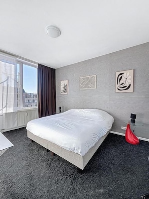 Habitación de hotel con una cama grande, una ventana con cortinas y obras de arte en la pared.