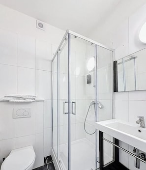 Un baño moderno con cabina de ducha de vidrio, un lavamanos blanco y un inodoro.