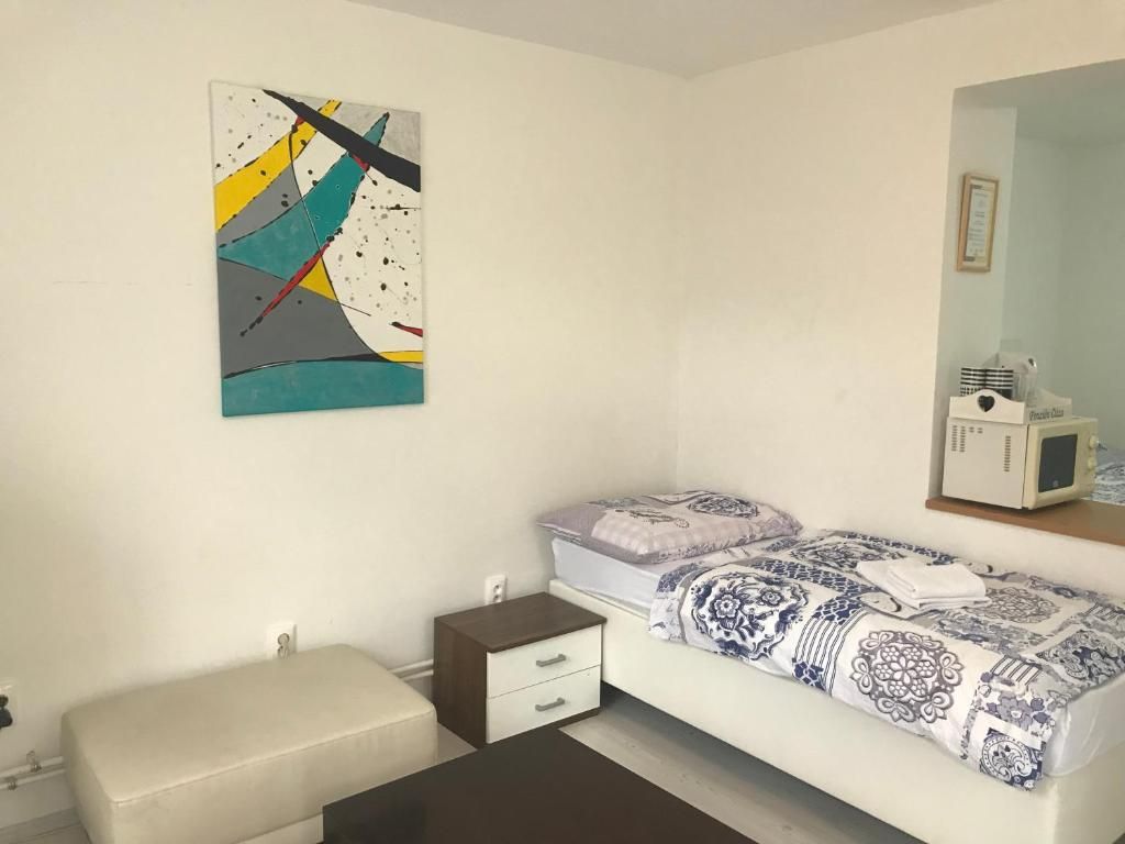 A bedroom with a bed, a bedside table, a nightstand, a wall-mounted TV, and a painting.