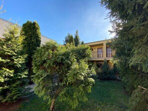 A residential building with a two-story structure, surrounded by dense greenery and a well-maintained lawn.