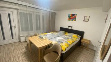 Quarto com cama, mesa, cadeira e janela com cortinas.