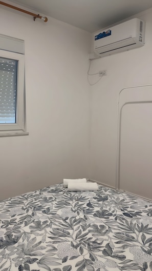Et værelse med en seng, et klimaanlæg, et vindue med skodder og en radiator på væggen.