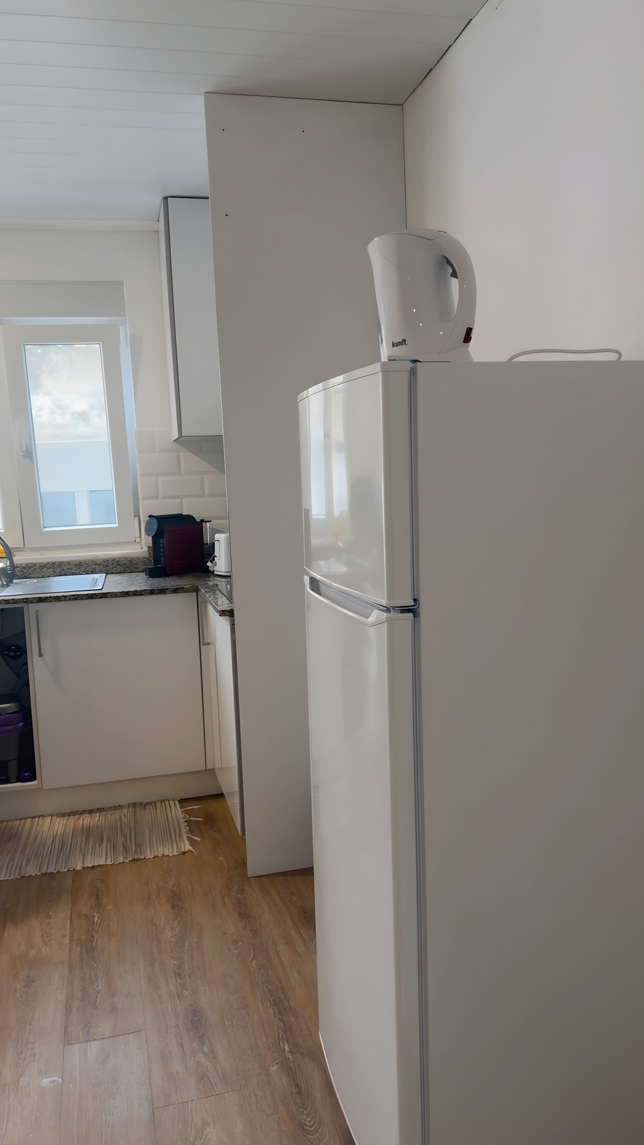 Cocina con refrigerador blanco, ventana y piso de madera.