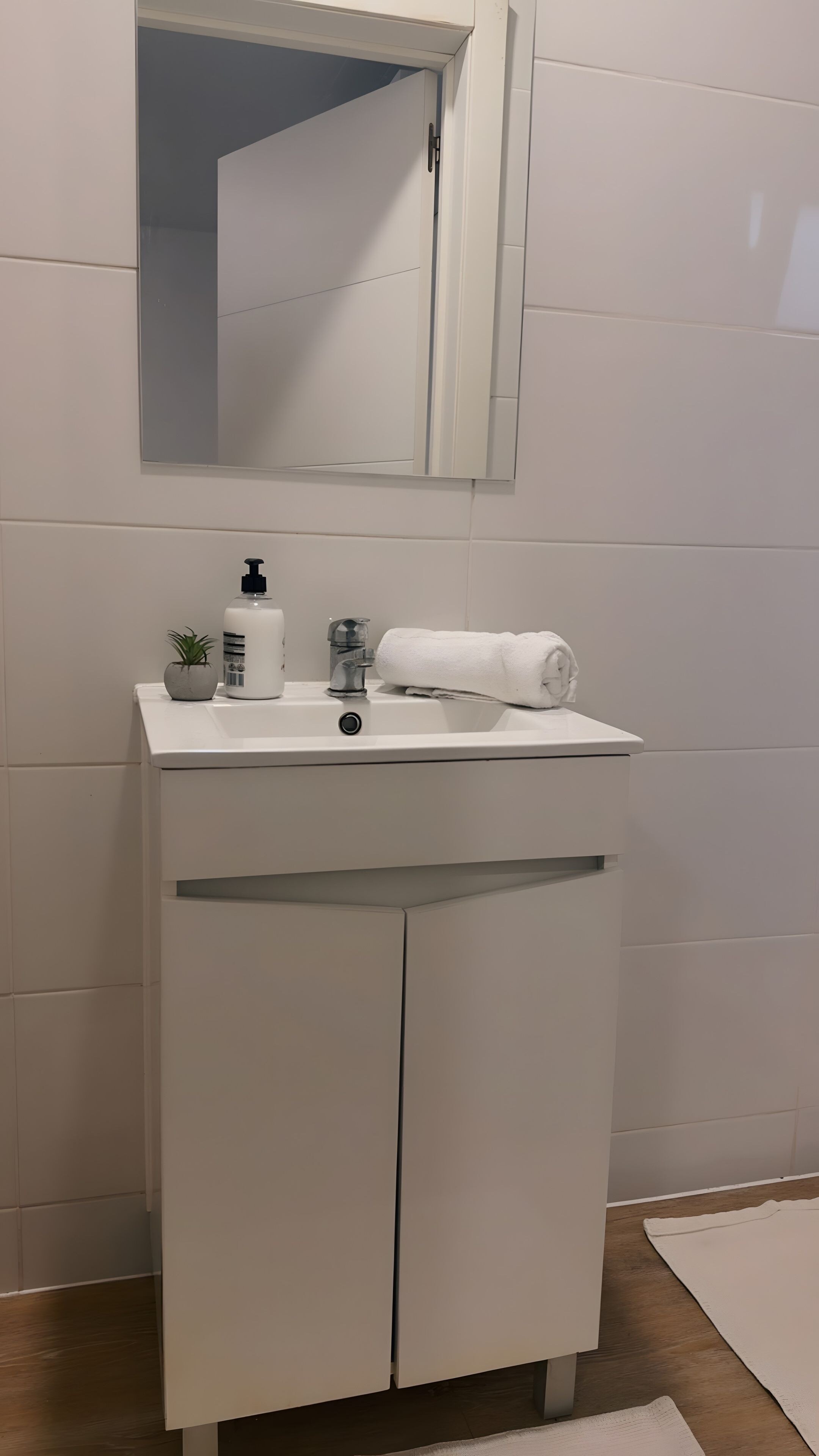 Ein Badezimmer mit einem weißen Waschbecken, einem Spiegel, einem Handtuch, einer Seifenspender und einer kleinen Pflanze.