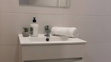 Ein Badezimmer mit einem weißen Waschbecken, einem Spiegel, einem Handtuch, einer Seifenspender und einer kleinen Pflanze.