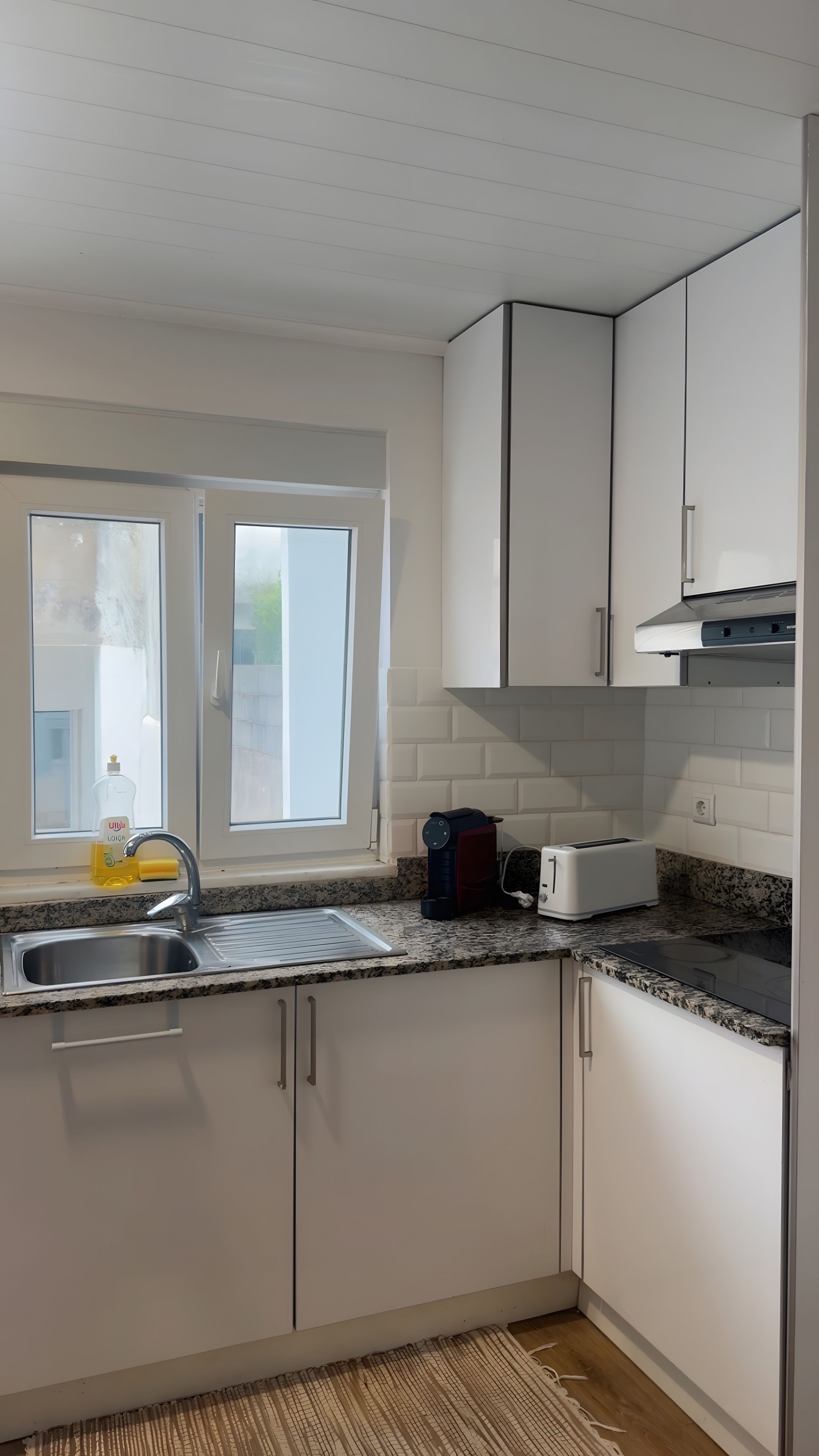 A modern kitchen with white cabinets, a granite countertop, a built-in oven, and a window providing natural light.