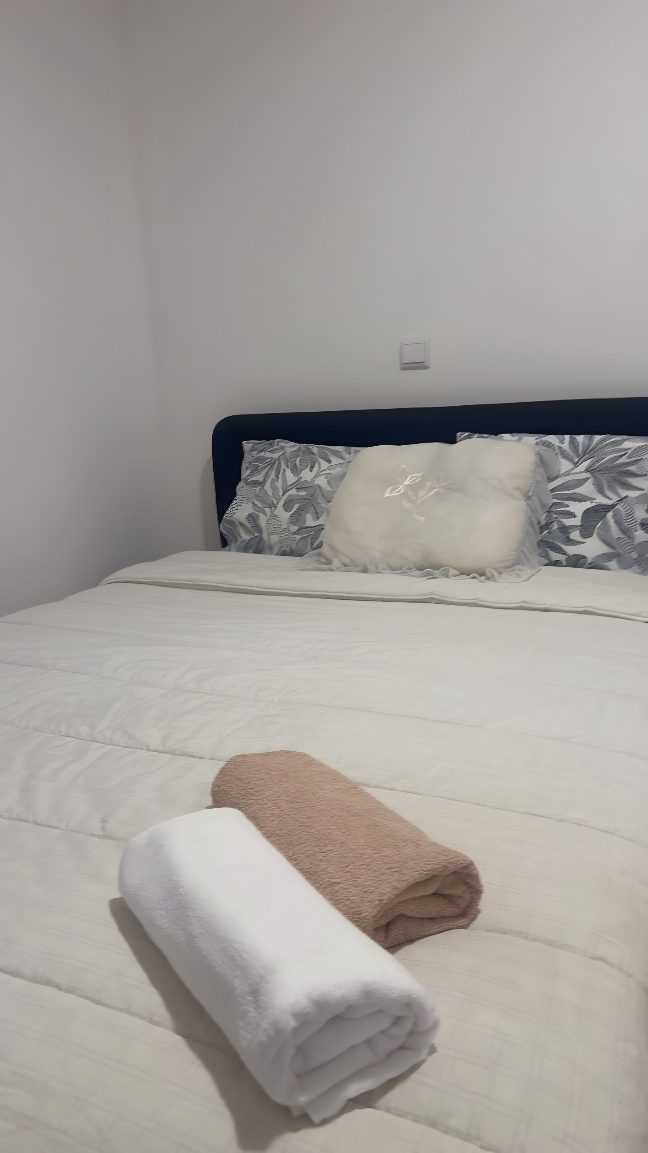 A bed with a white quilt, a beige towel, and patterned pillows.