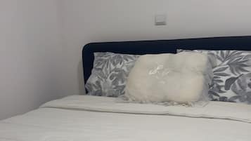 A bed with a white quilt, a beige towel, and patterned pillows.