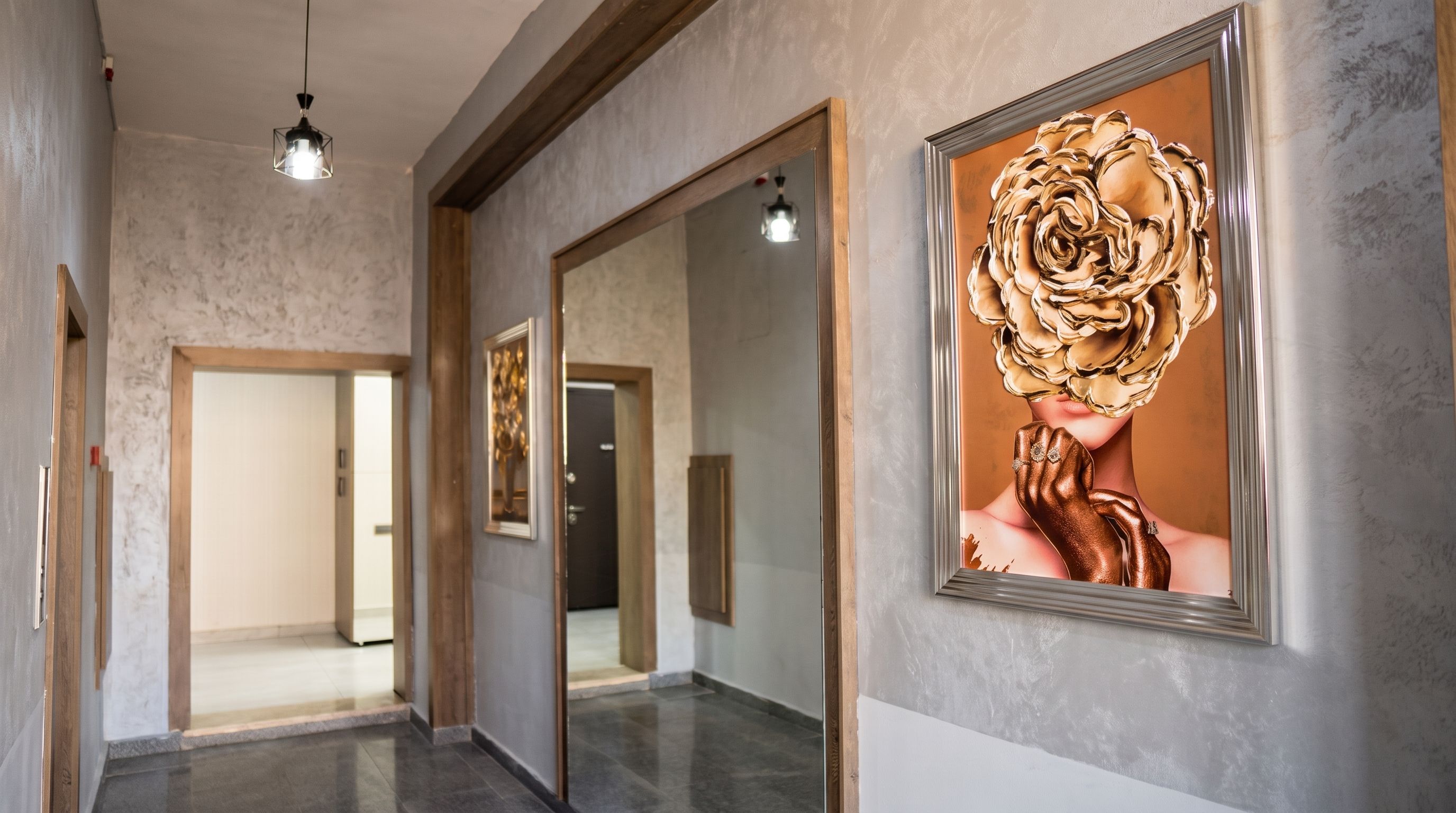 Un couloir avec un miroir qui reflète une pièce, une œuvre d’art encadrée accrochée au mur et un luminaire suspendu au plafond.