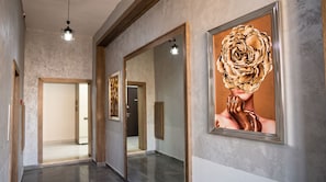 A hallway with a mirror reflecting a room, a framed artwork on the wall, and a hanging light fixture. - Alivium Apartments Baku (Bakı)