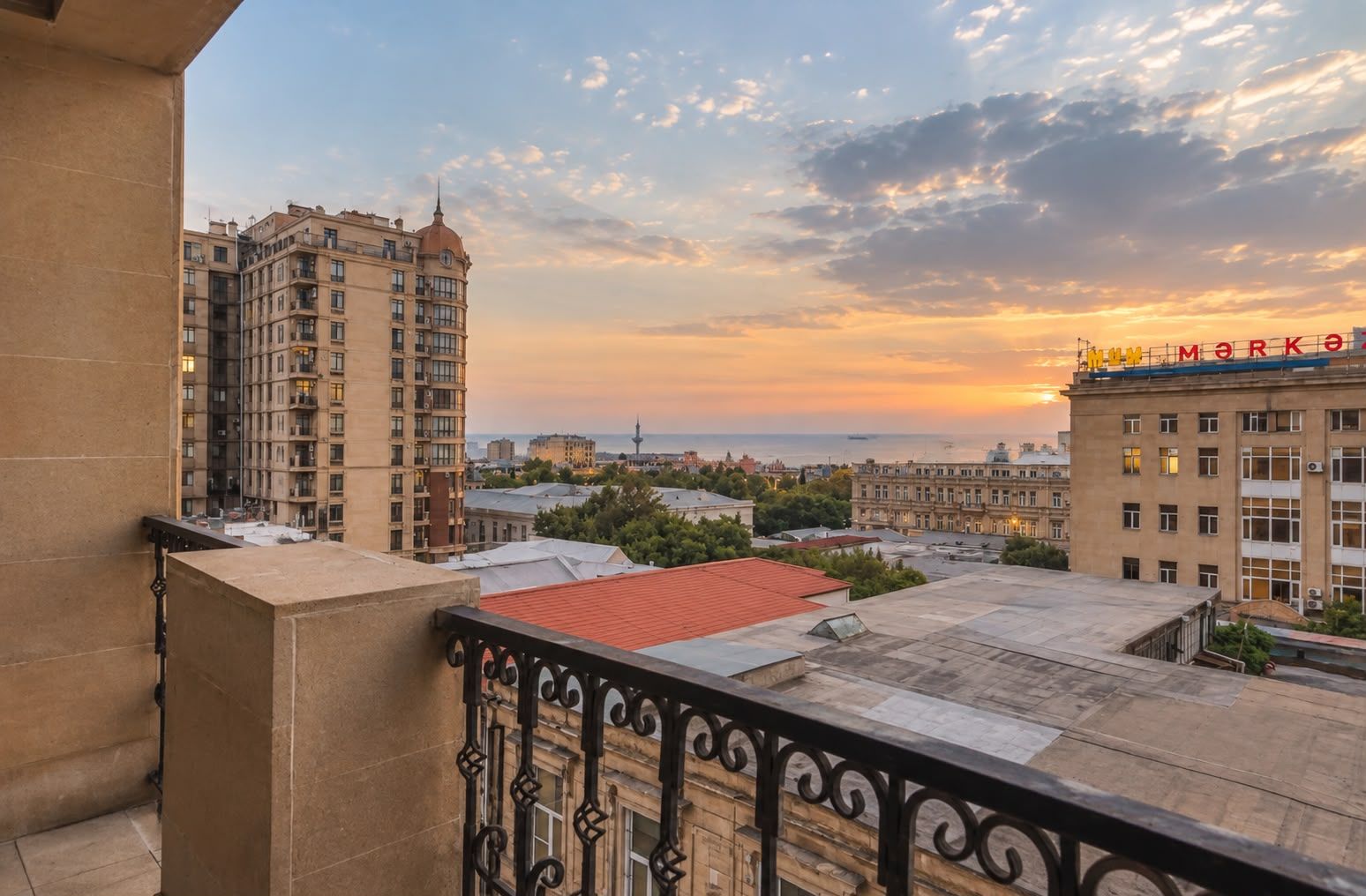 Un balcon orné d’une balustrade en fer forgé, d’où l’on peut admirer un panorama urbain au coucher du soleil.