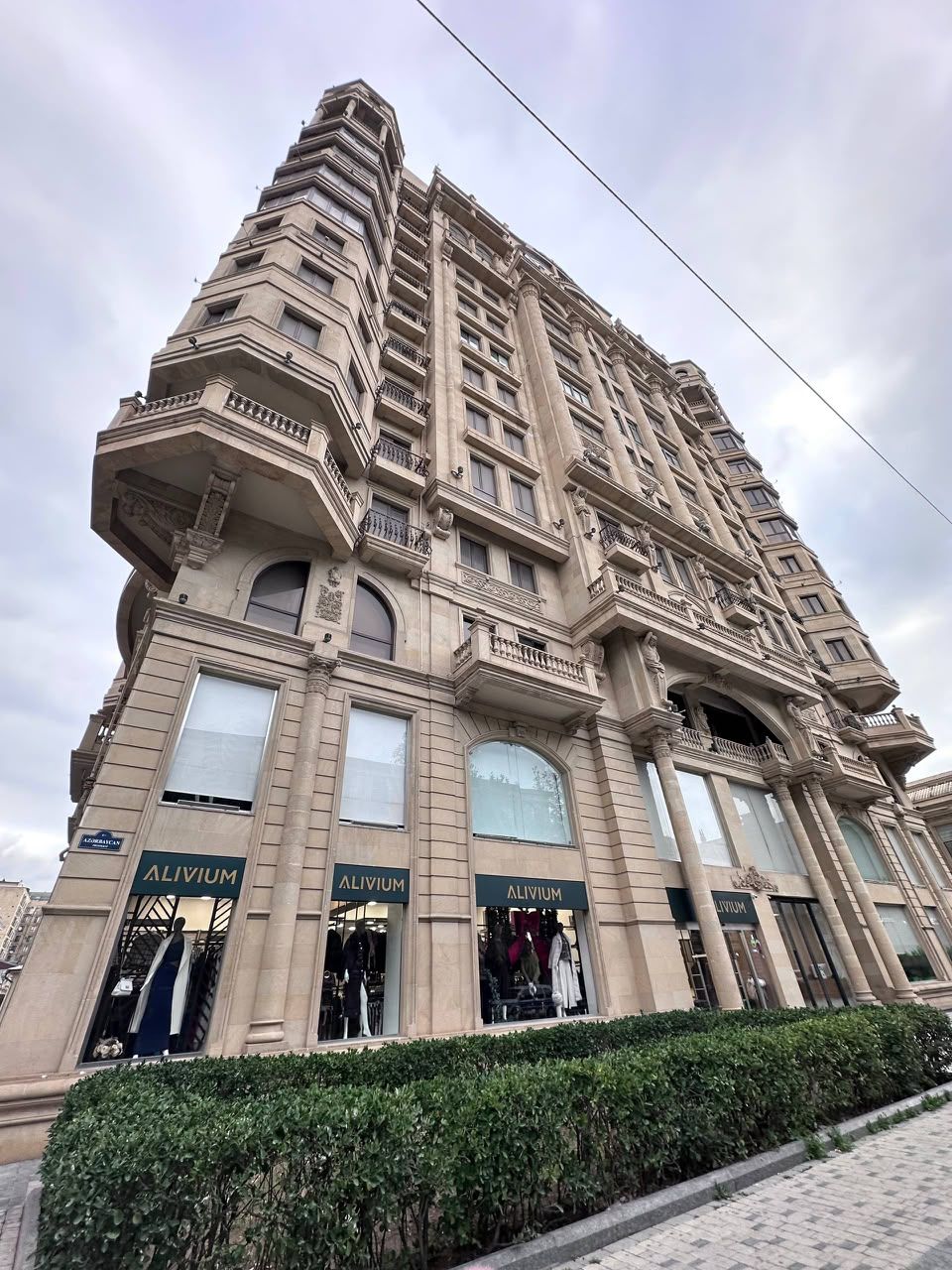 Un immeuble à plusieurs étages, doté de balcons et de grandes fenêtres, avec des devantures de magasins arborant l’enseigne « ALIVIUM ».
