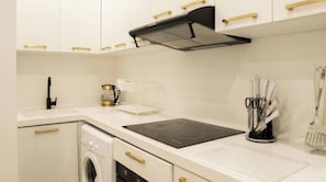 Una cocina moderna con armarios blancos, una placa de inducción negra, una cafetera y un recipiente para utensilios.