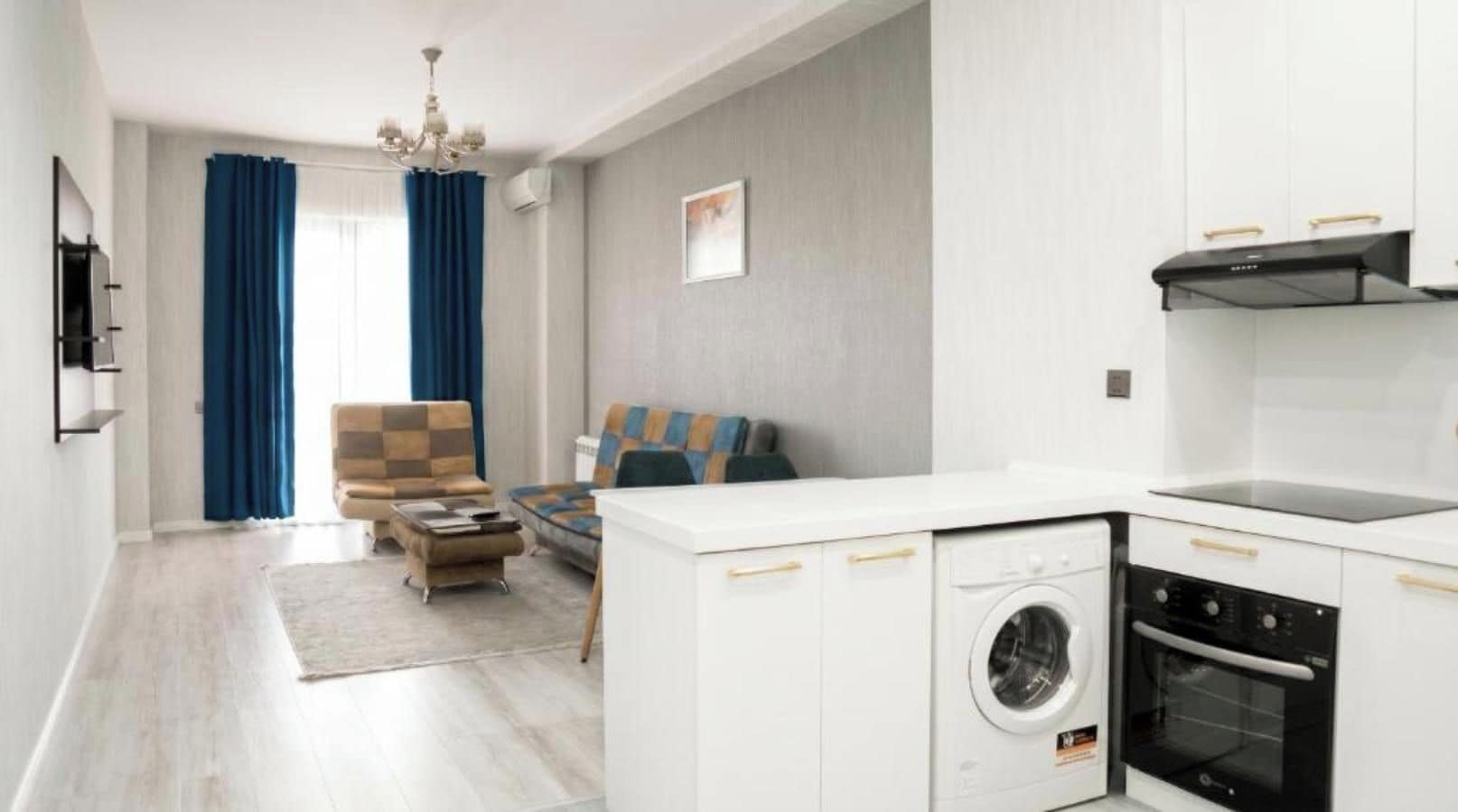 A modern apartment with a kitchen, a living area with a sofa and armchair, and a laundry area with a washing machine and dryer.