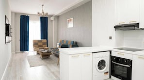 A modern apartment with a kitchen, a living area with a sofa and armchair, and a laundry area with a washing machine and dryer. - Alivium Apartments Baku (Bakı)