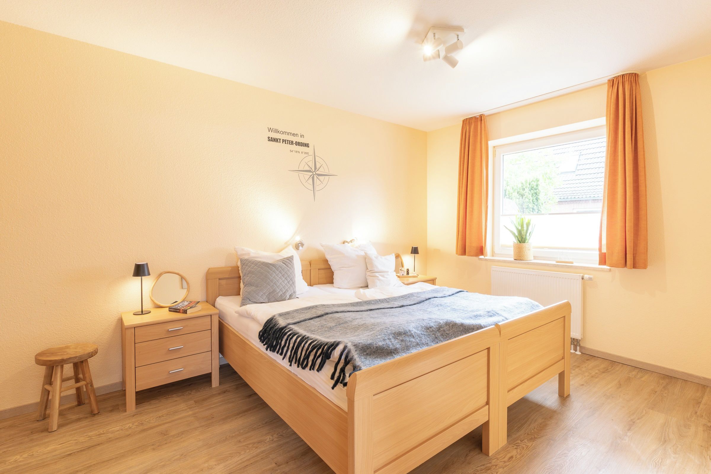 Ein Schlafzimmer mit einem Bett, Nachttischen, einer Fensterbank und einem an der Wand befestigten Kompass.