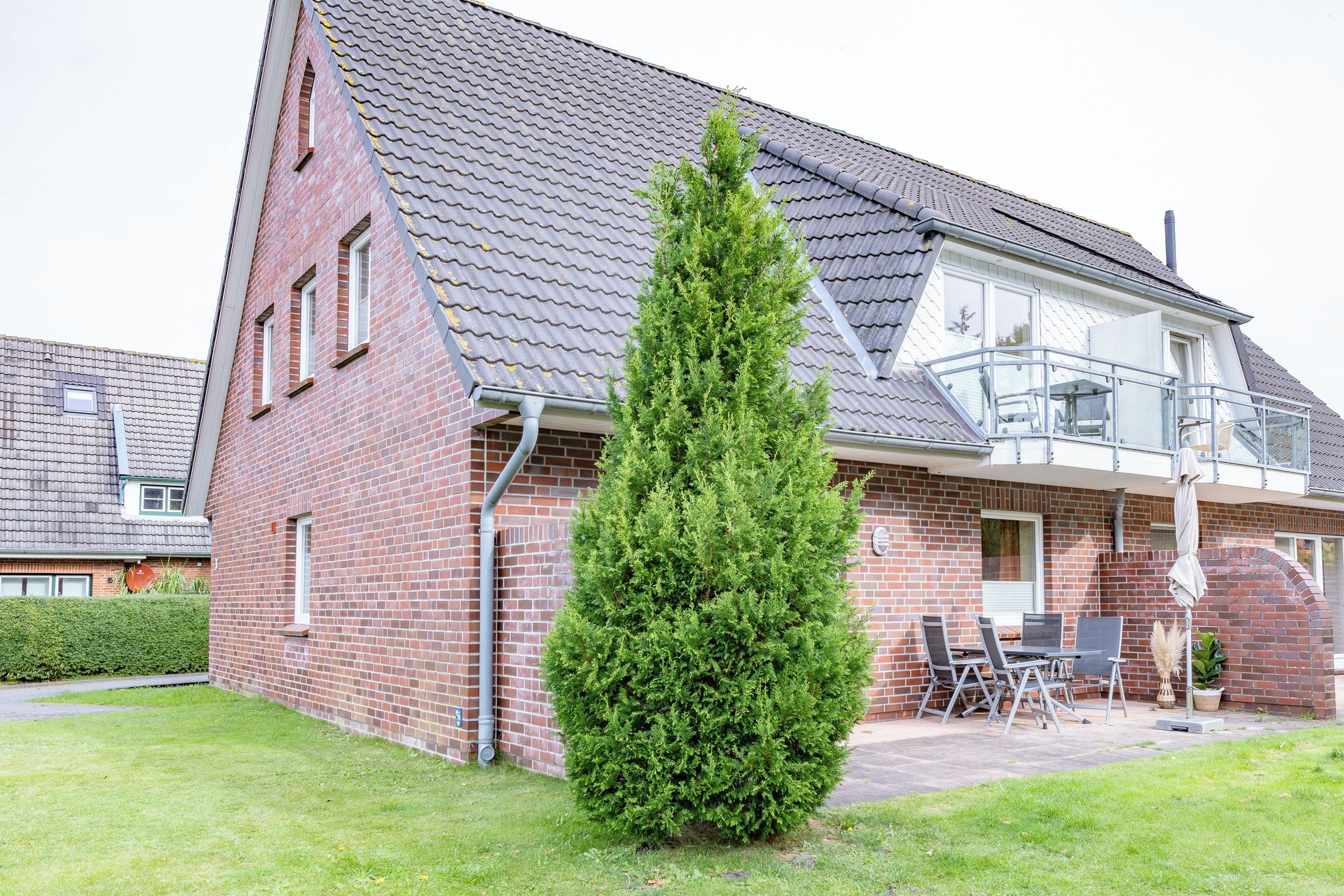 Ein zweistöckiges Haus mit Ziegelverkleidung, einem Ziegeldach und einem kleinen Balkon mit Gartenmöbeln.