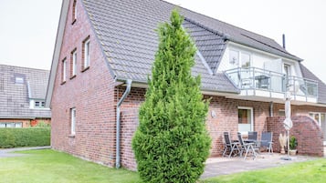 Ein zweistöckiges Haus mit Ziegelverkleidung, einem Ziegeldach und einem kleinen Balkon mit Gartenmöbeln.
