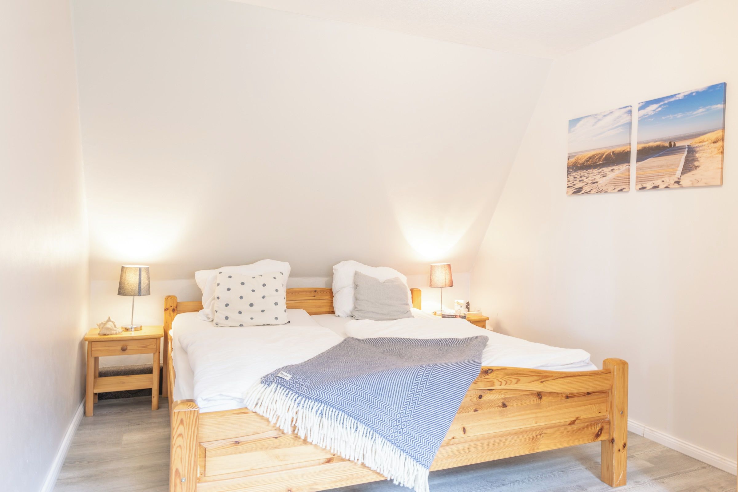 Une chambre à coucher avec un lit en bois, deux tables de chevet, une petite table et une lampe fixée au mur.