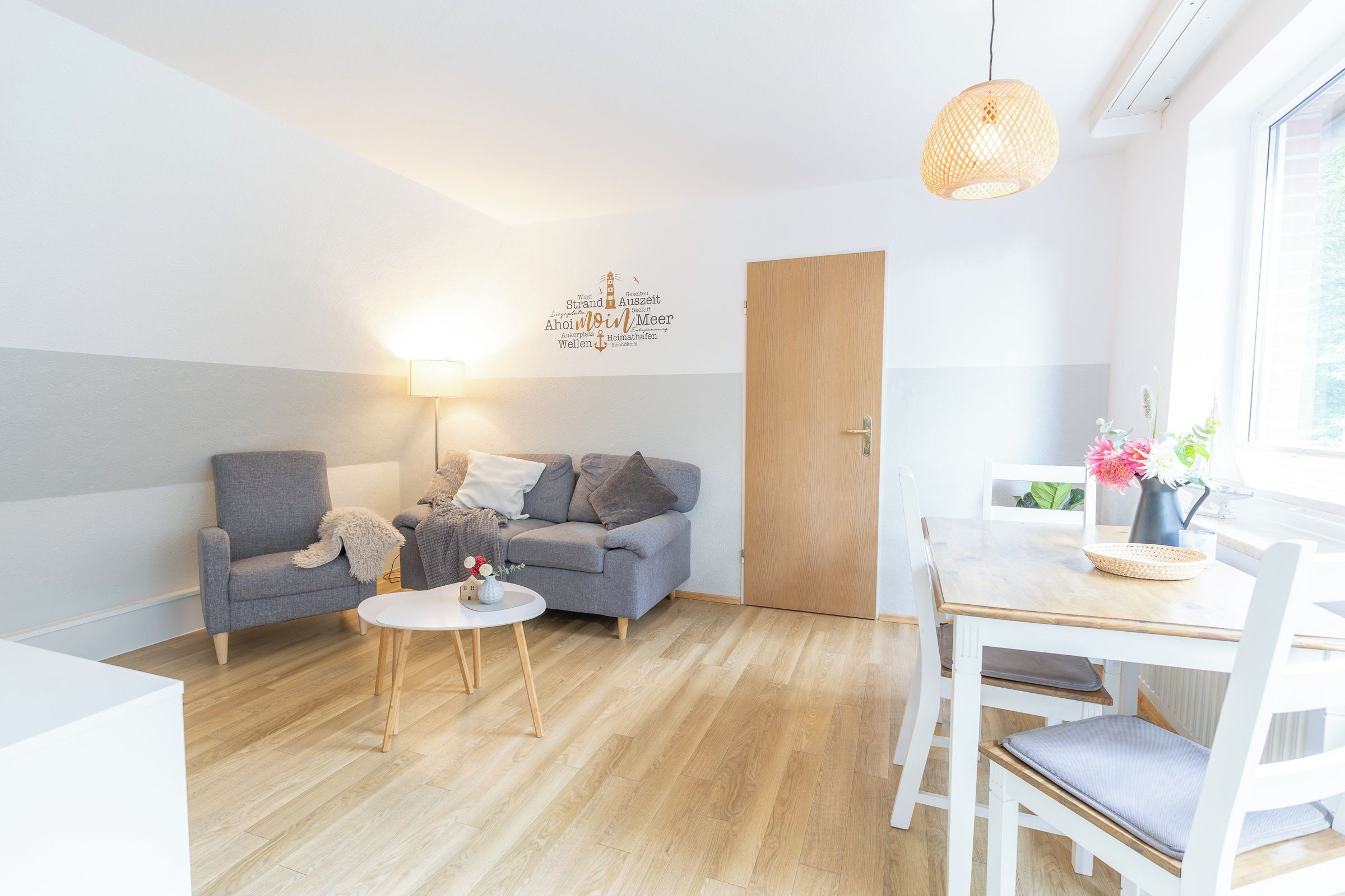 Una sala moderna con un sofá gris, una mesita redonda y una mesa de comedor de madera con sillas.