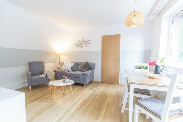 Una sala moderna con un sofá gris, una mesita redonda y una mesa de comedor de madera con sillas.