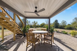 A covered outdoor seating area with a table and chairs, a ceiling fan, and a staircase.