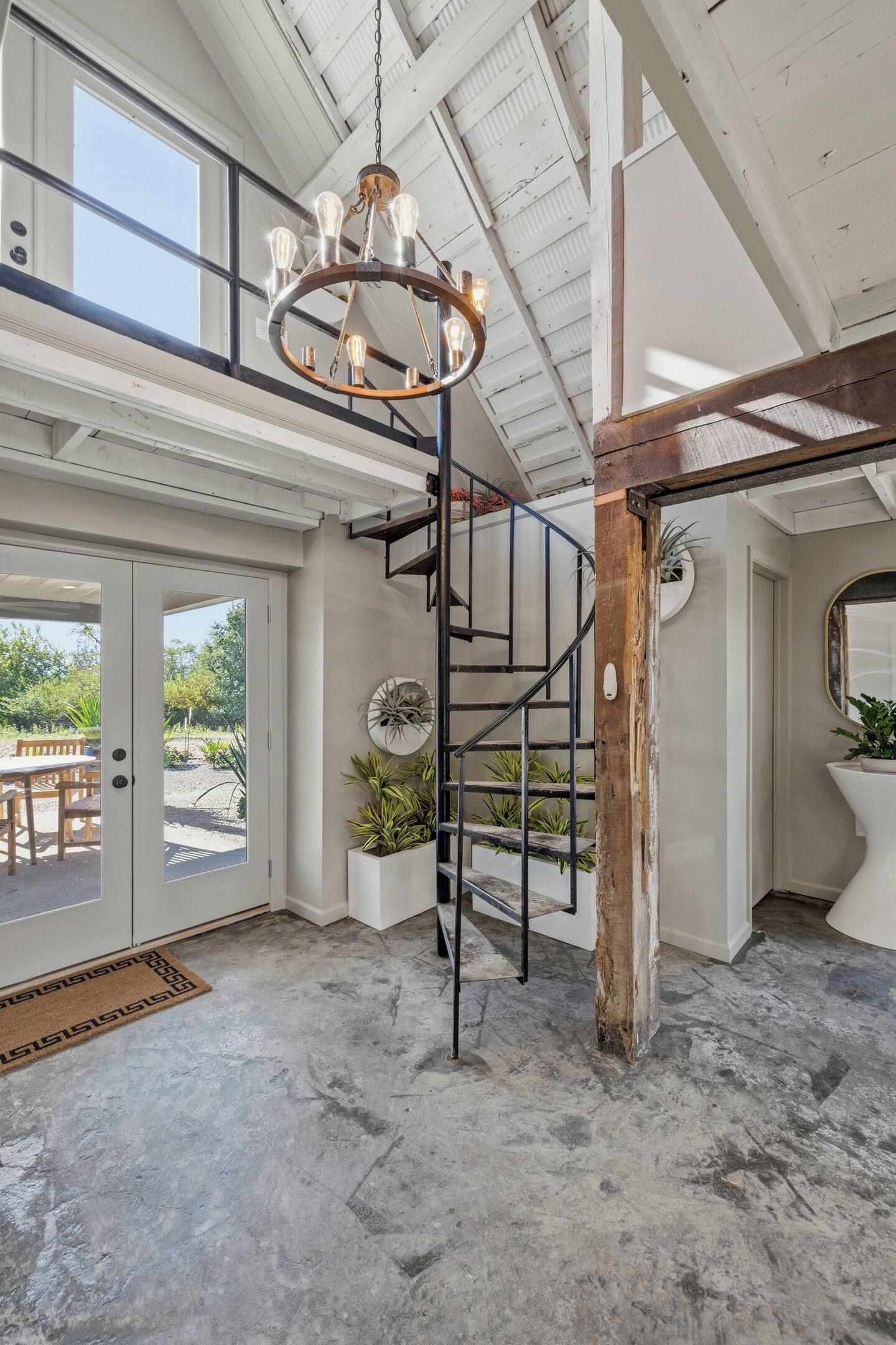 Un intérieur spacieux avec un escalier central, un lustre et une vue sur l’extérieur grâce à une porte vitrée.
