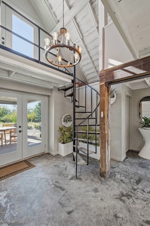 Ein geräumiges Interieur mit einer zentralen Treppe, einem Chandelier und Blick durch eine Glastür.