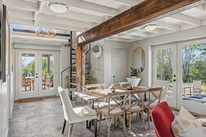 A dining area with a round table, chairs, and a red chair. There is a staircase leading to an outdoor area.
