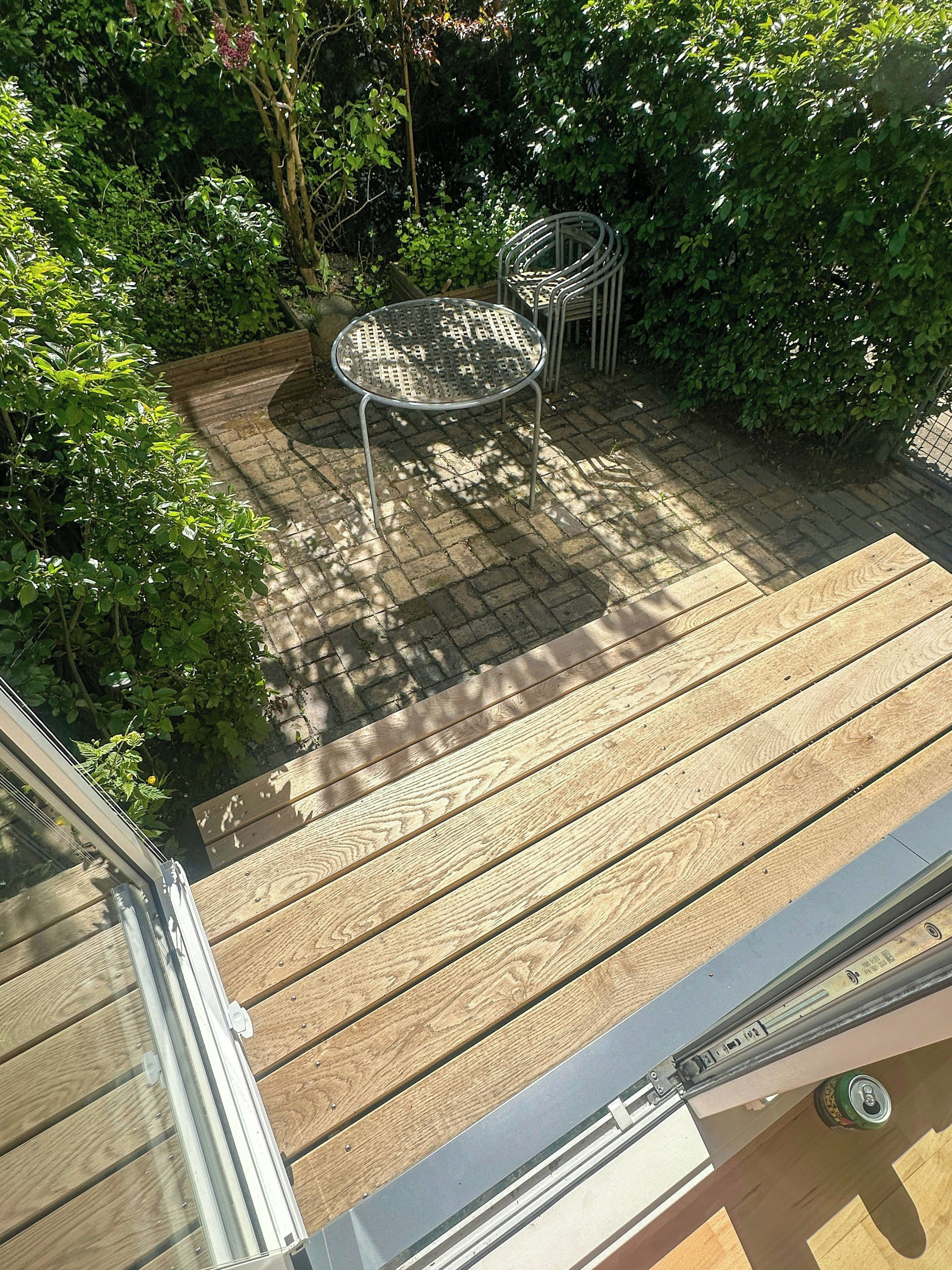 Una terraza de madera con una mesa y silla de metal, rodeada de follaje.