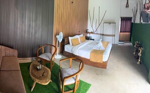 A bedroom with a bed, two chairs, a small table, a fan, and a green wall with decorative branches. - 7 Art Villa (ELLA)