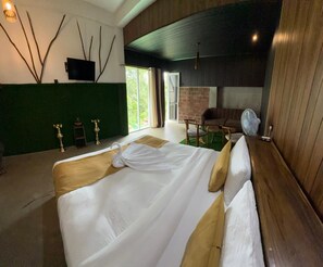 A hotel room with a bed, a television, a brick wall, a fan, and a view of greenery outside. - 7 Art Villa (ELLA)