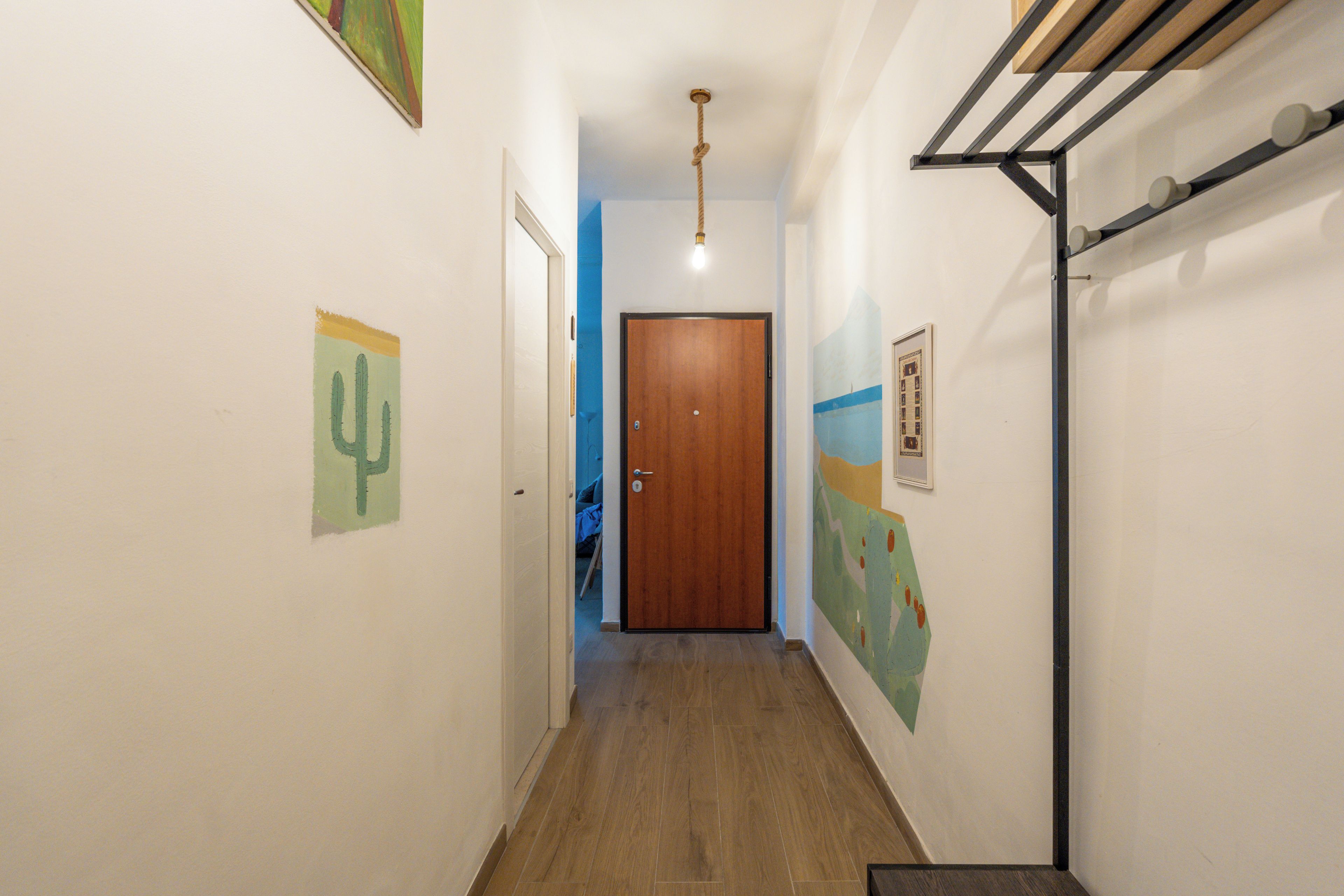 A hallway with a wooden door at the end, a ceiling light, and wall-mounted artwork.