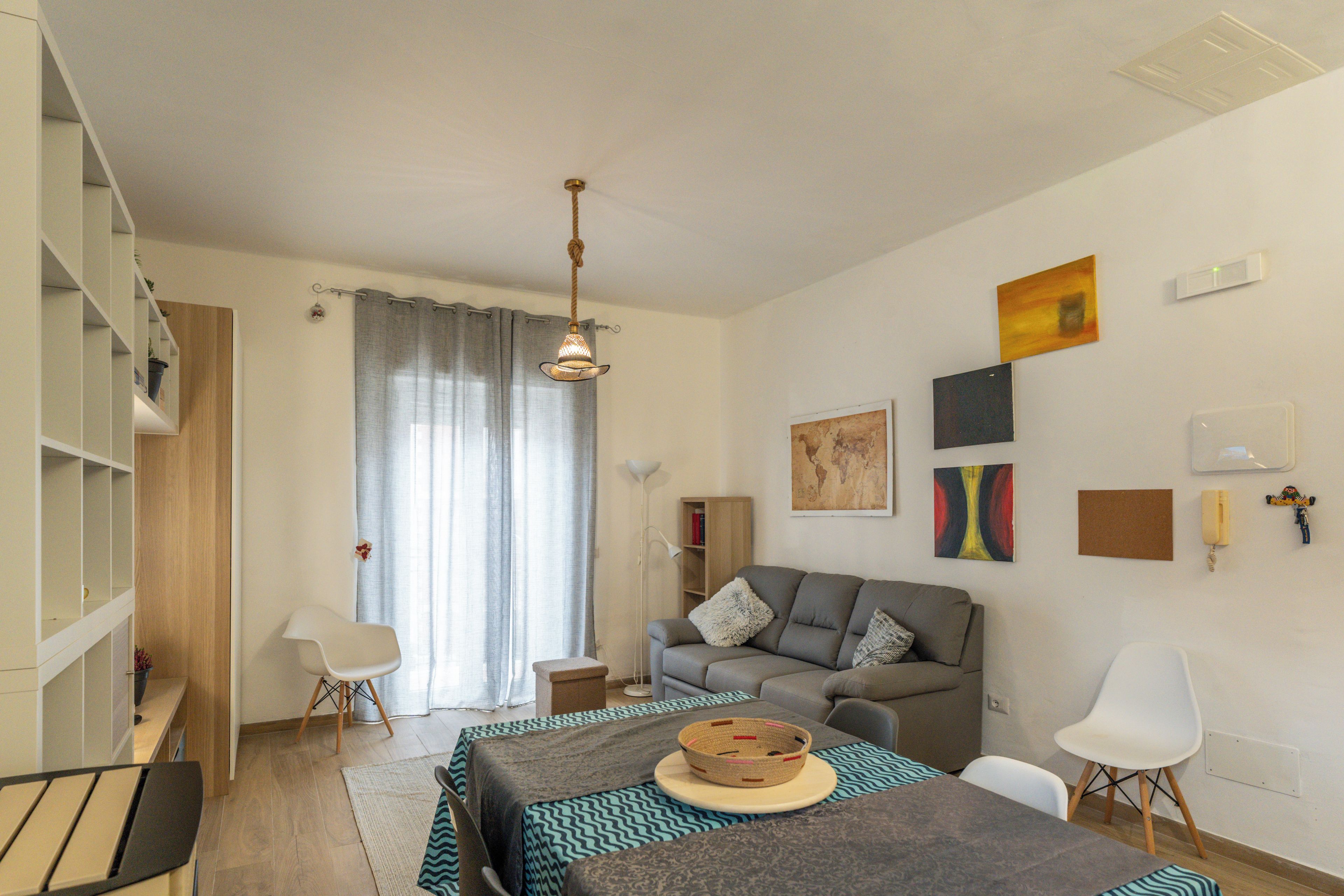 A modern living room with a sofa, a dining table, and a coffee table. There are bookshelves and a lamp.
