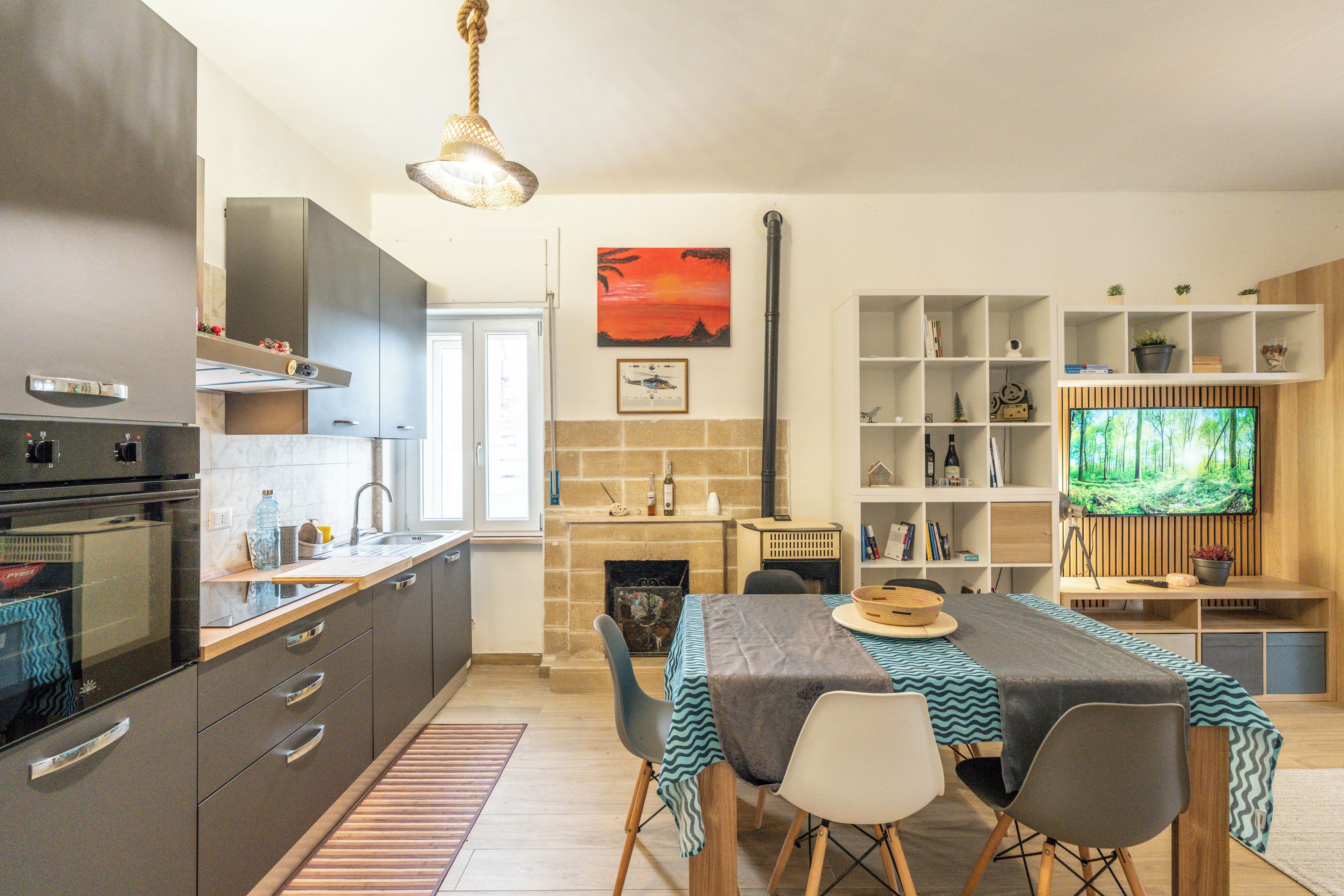 Une cuisine moderne dotée d’un four encastré, un coin repas avec une table et des chaises, une cheminée et un téléviseur fixé au mur.