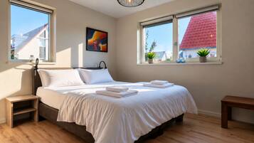 Een slaapkamer met een bed, nachtkastjes, een raam met uitzicht op gebouwen en een schilderij aan de muur.
