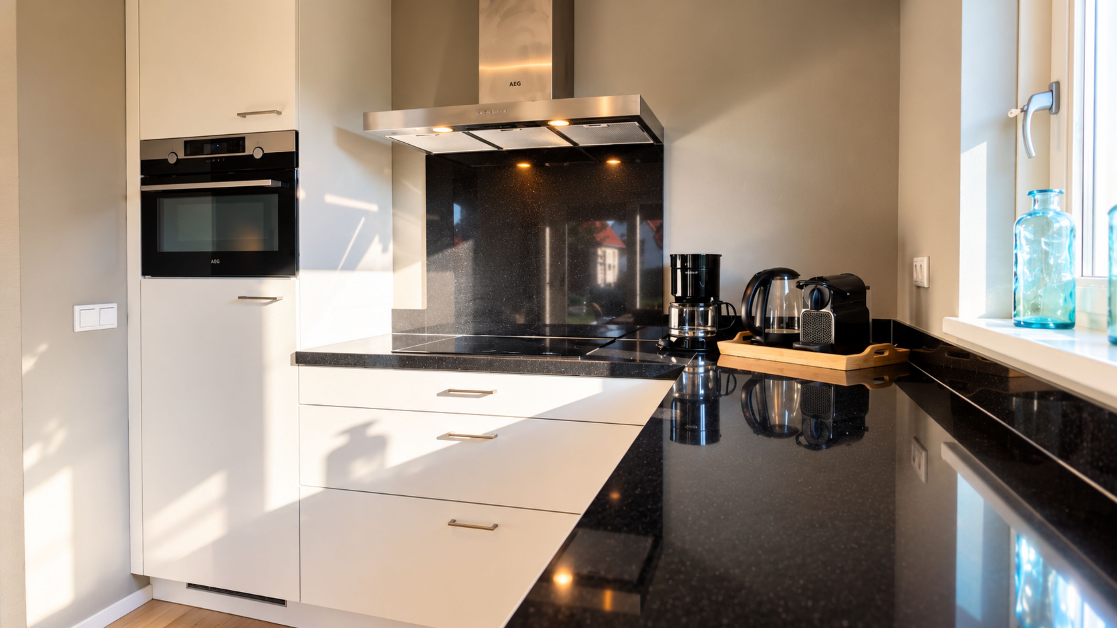 A modern kitchen with a built-in oven, a range hood, a coffee maker, and a window with a view.