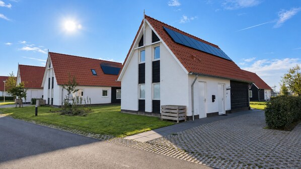 A row of white buildings with red roofs and solar panels, a paved driveway, and a clear sky.