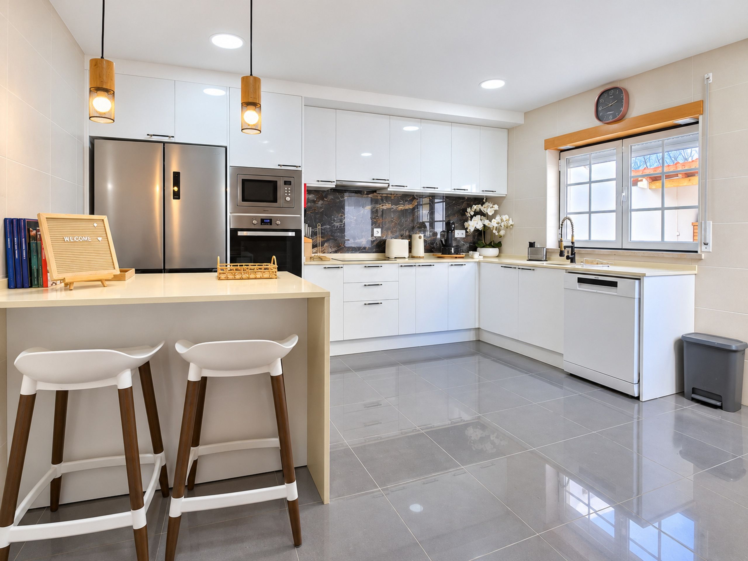 A modern kitchen with white cabinets, stainless steel appliances, and a wooden bar area with two white stools.