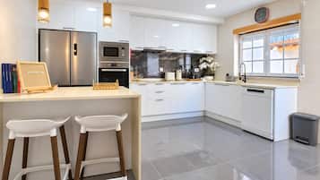 A modern kitchen with white cabinets, stainless steel appliances, and a wooden bar area with two white stools.