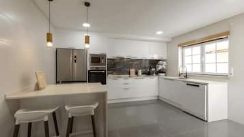 A modern kitchen with white cabinetry, a stainless steel refrigerator, a built-in oven, and a large island with bar stools.