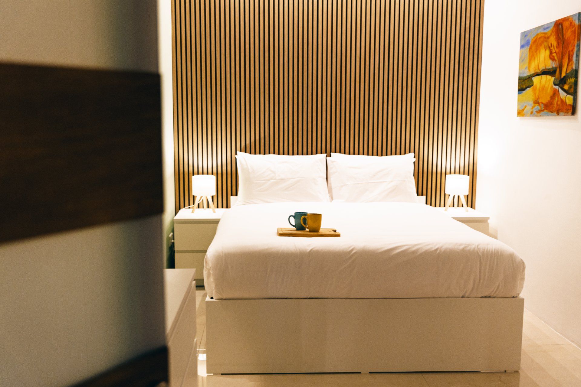 A hotel room with a bed, bedside tables, and a painting on the wall.