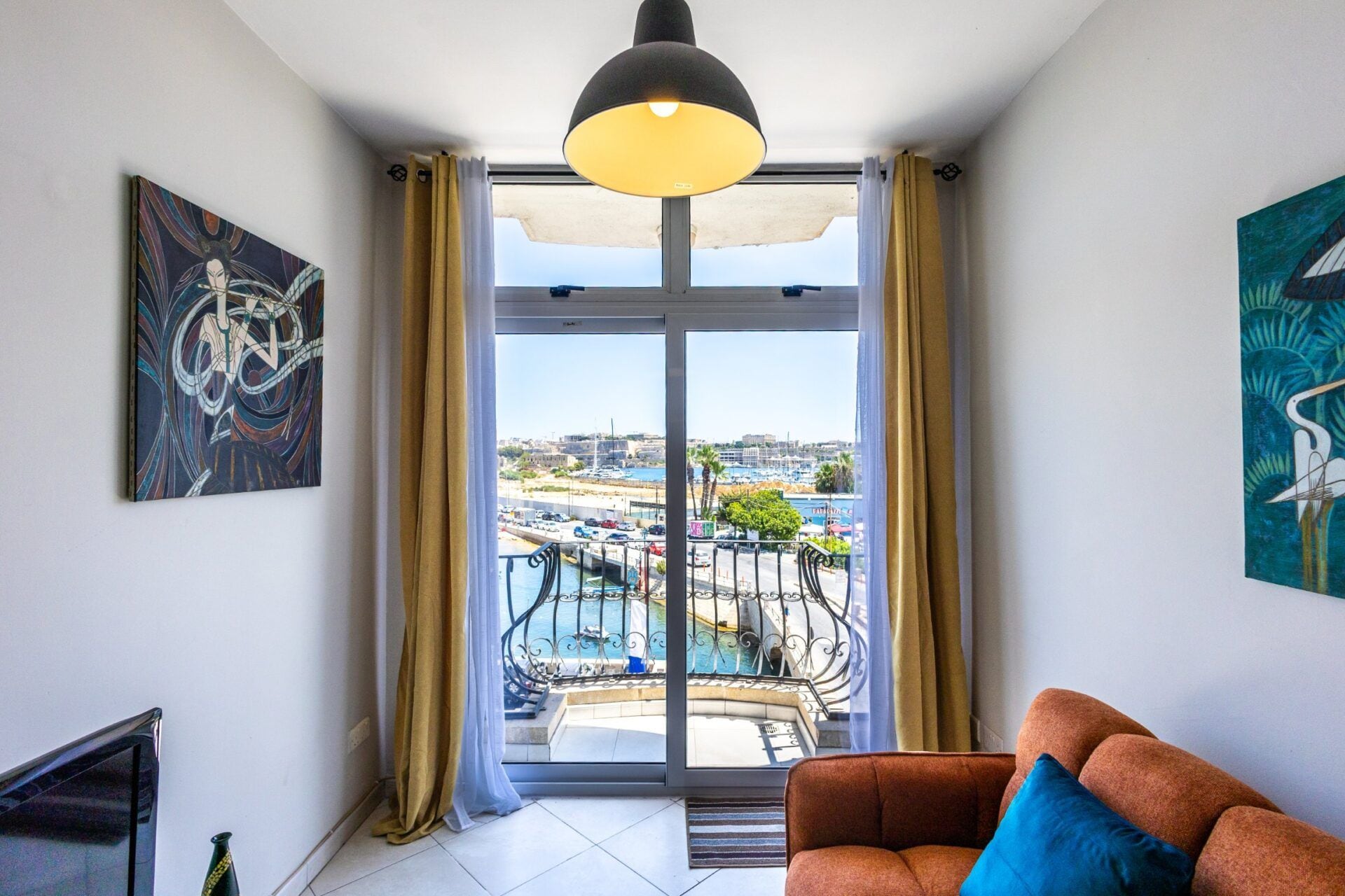 A living room with a sofa, a painting, and a view of a pool and cityscape through large windows.