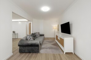 A modern living room with a grey sofa, a white entertainment unit, and a flat-screen TV. - GtHouse's Atlantic Coast Retreat   (Atouguia da Baleia)