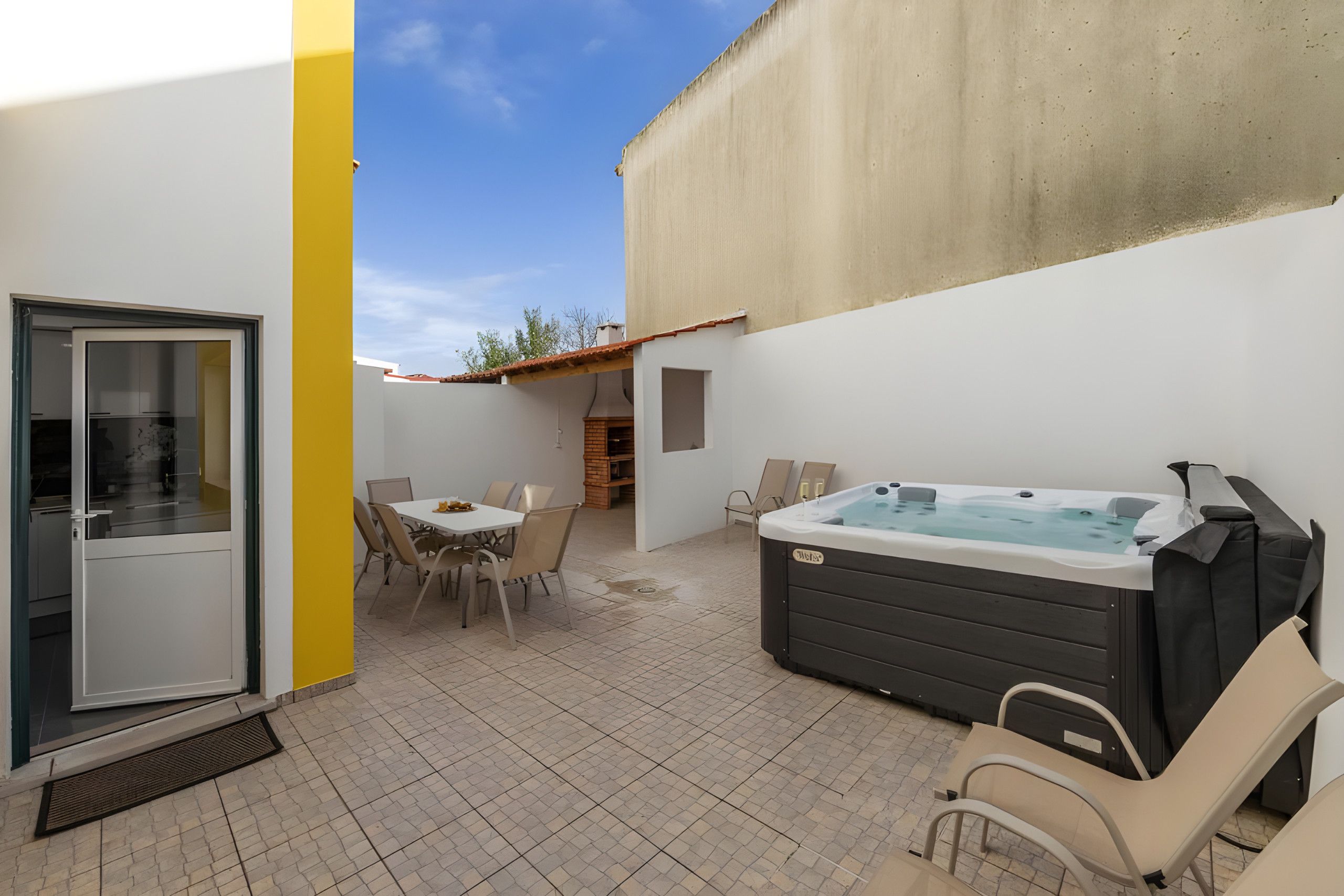 A patio area with a hot tub, outdoor seating, and a door leading to an interior space.