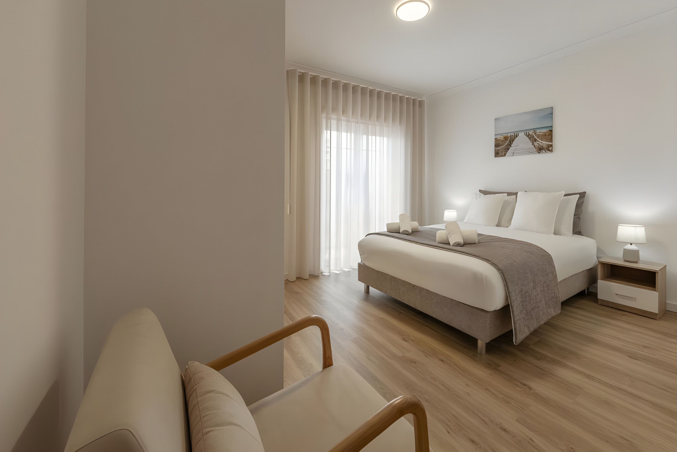 Une chambre d’hôtel moderne, équipée d’un lit, de tables de chevet, d’une chaise et d’un tableau au mur.